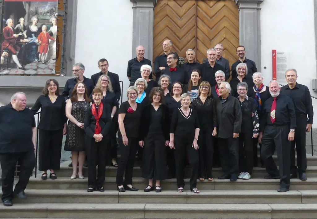 Das Orchestra Euterpe Bozen und das Tennenloher Zupforchester steht auf der Treppe des Haupteingangs des Merkantilgebäude in Bozen.